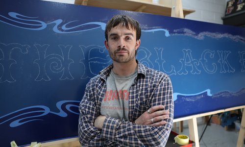 Lockie standing in front of an in progress handpainted sign