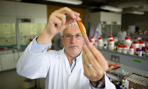 man in a white coat in a lab holding up a vial