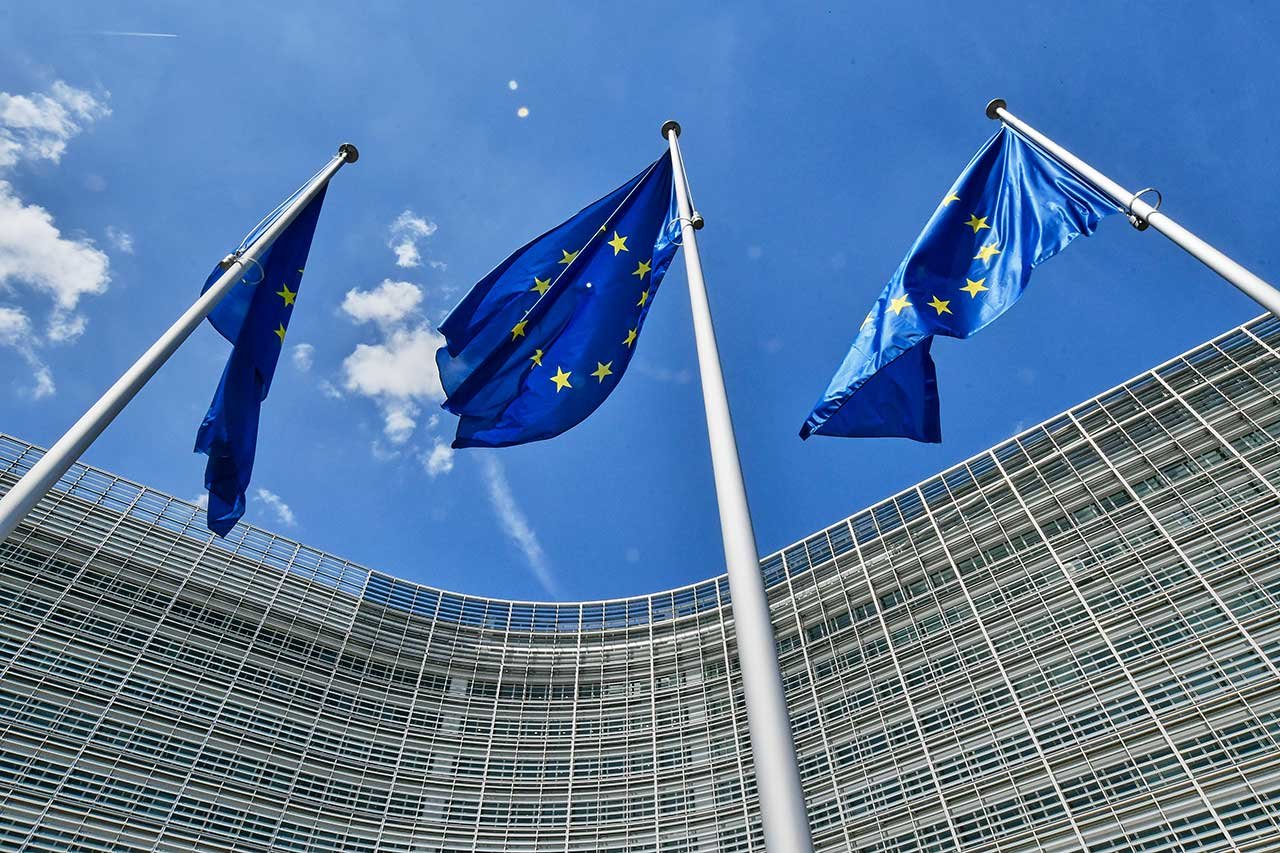 three tall EU flags in front of a business building