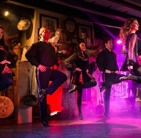 four irish dancers in the air with legs crossed in a dance with purple lighting behind them